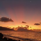 Tranquil seascape at twilight with full moon, sun, and orange sky