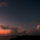 Starry night seascape with shooting stars and glowing house on shore