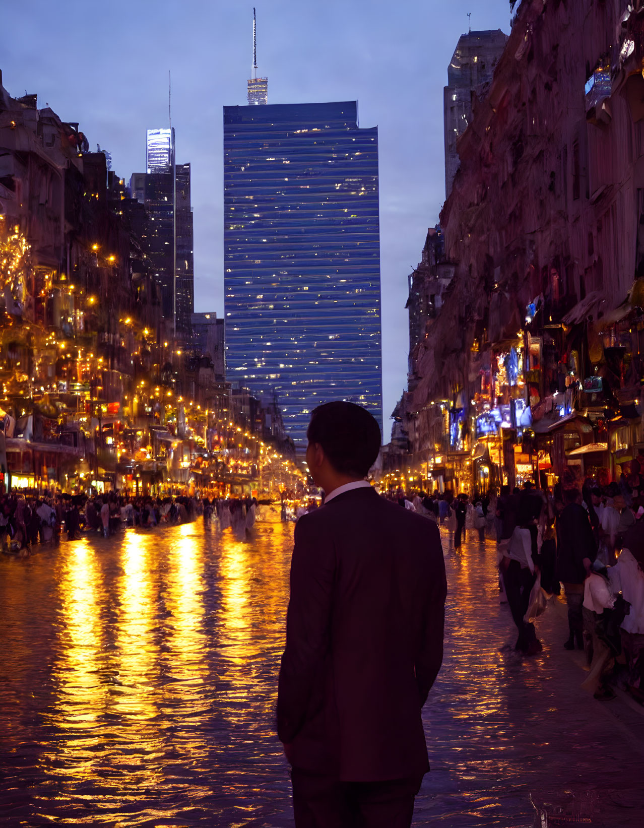 Businessperson in suit observing city street at dusk with illuminated building in background.