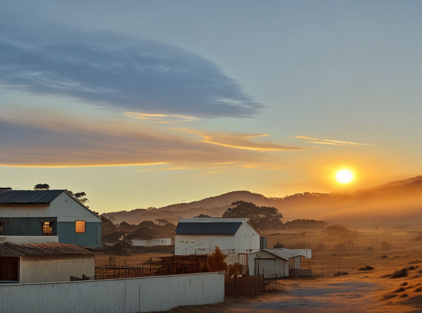 Serene sunrise over rural landscape with buildings, fence, and rolling hills