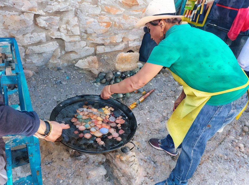 Person cooking colorful sweets in large pan at outdoor stall.