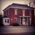 Red brick two-story house with white trim and porch at twilight.