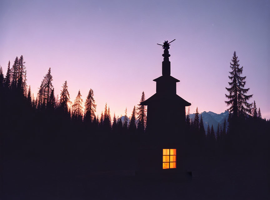 Chapel silhouette with lit window, twilight sky, pines, mountains