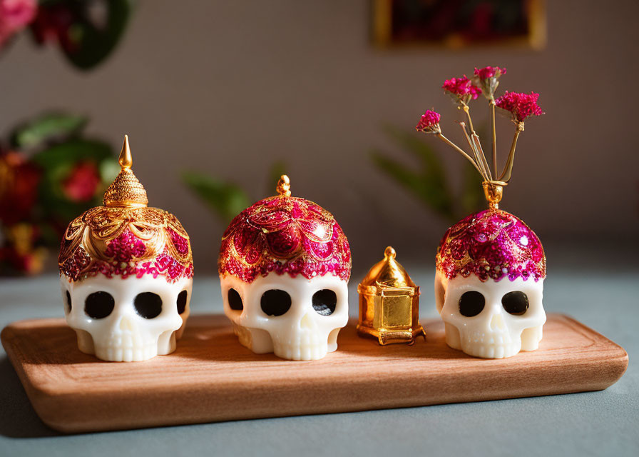 Intricate pink and gold skull figurines with gold lantern on wooden tray