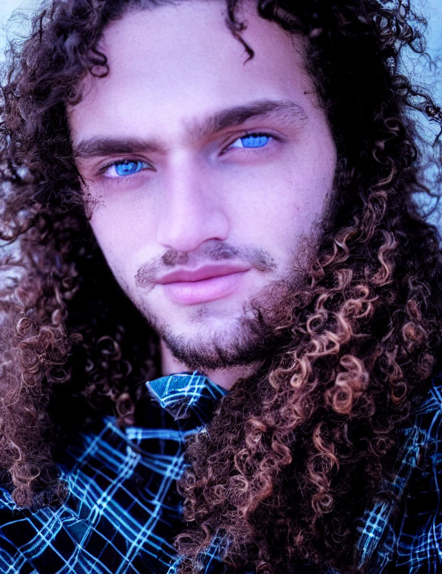 Close-up portrait of person with curly hair and blue eyes in checkered shirt
