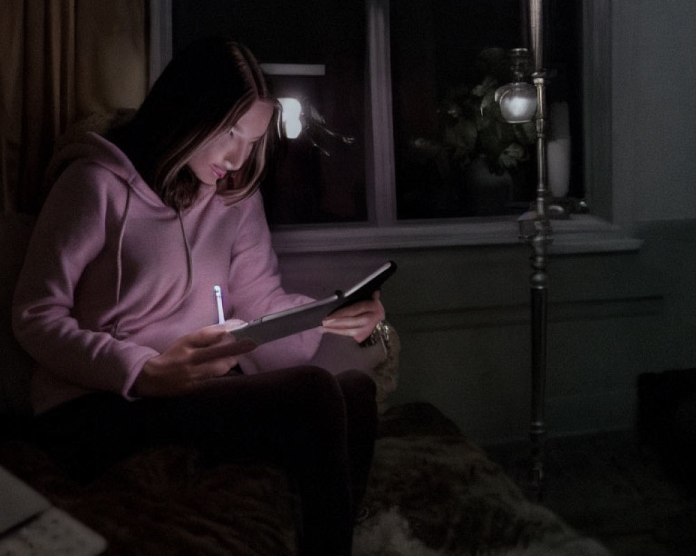 Person in Pink Hoodie Writing Near Window at Night
