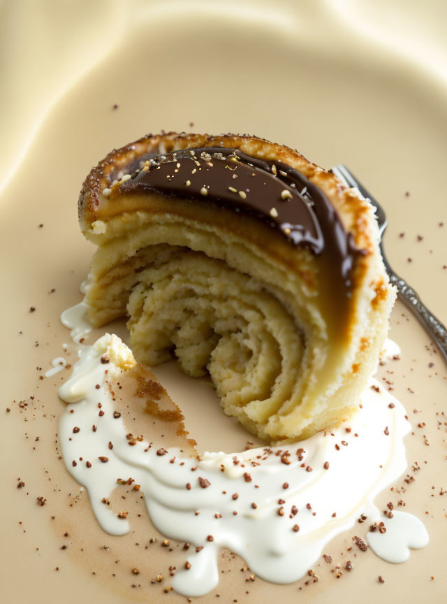 Rolled cake with chocolate glaze, cream, and shavings on beige plate