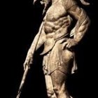 Warrior statue in ornate armor with spear on dark background