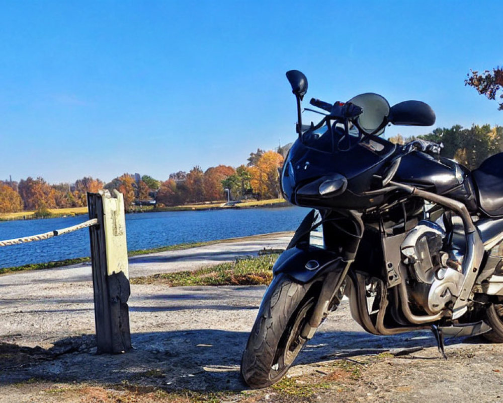 Motorcycle parked by serene lake with autumn trees and clear blue skies