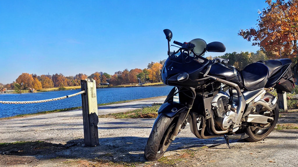 Motorcycle parked by serene lake with autumn trees and clear blue skies