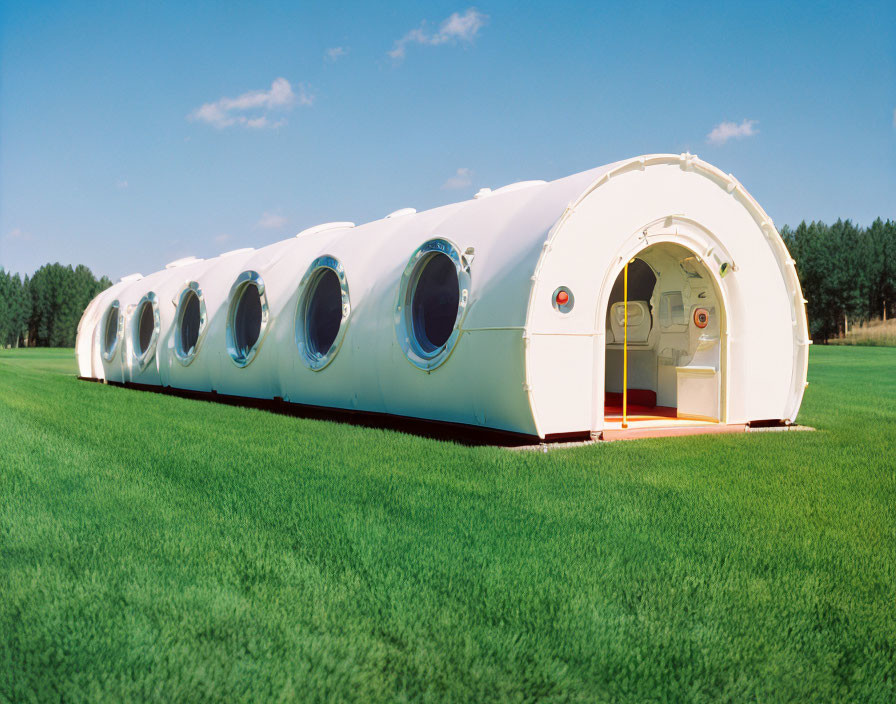 Futuristic white modular structure with circular windows on green lawn