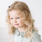 Smiling young girl with curly blonde hair in floral headpiece and cream dress