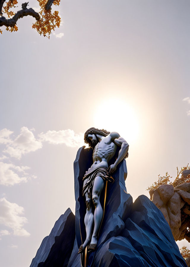 Muscular figure sculpture with draped cloth under sunny sky on blue rocks.