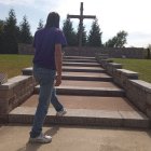 Person in Blue Cloak Ascending Outdoor Steps to Large Cross