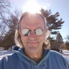 Curly Haired Man in Sunglasses with Sunburst in Snowy Landscape