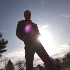 Bearded man holding cosmic orb with mountain landscape and sun