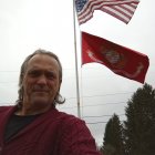 Regal figure with sun halo in purple cloak, flagpole with emblem, clouds and trees