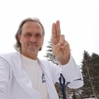 Serene man in white robe raises cross against stormy sky