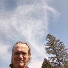 Winged figure statue with warrior beneath, set against blue sky and trees