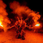 People in demon costumes engulfed in flames and smoke at night.