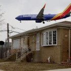 Vibrant airplane flying over suburban house with white car on cloudy day