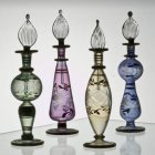 Four ornate glass oil lamps with intricate floral designs on light background