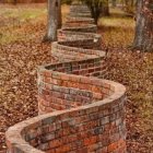 Brick wall winding through serene forest with sunlight filtering.