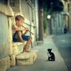 Child blowing dandelion on sunny stairway with curious cats, greenery, and classical architecture.