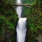 Tranquil waterfall in forested canyon with bridge and lush greenery