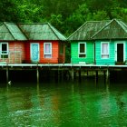 Stilt houses over water with lush green hills and wooden boats under overcast sky