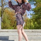 Woman in patterned crop top and shorts with straw hat on steps.