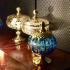 Three ornate gold-accented perfume bottles on glossy surface with mosaic background