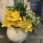 Vibrant painting of golden yellow flowers in a white vase surrounded by lush green and blue foliage