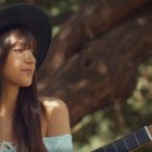 Two women playing guitars in a mystical forest with warm sunlight.