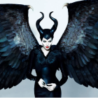 Person in dramatic black costume with iridescent blue-black wings and horned headpiece against pale background