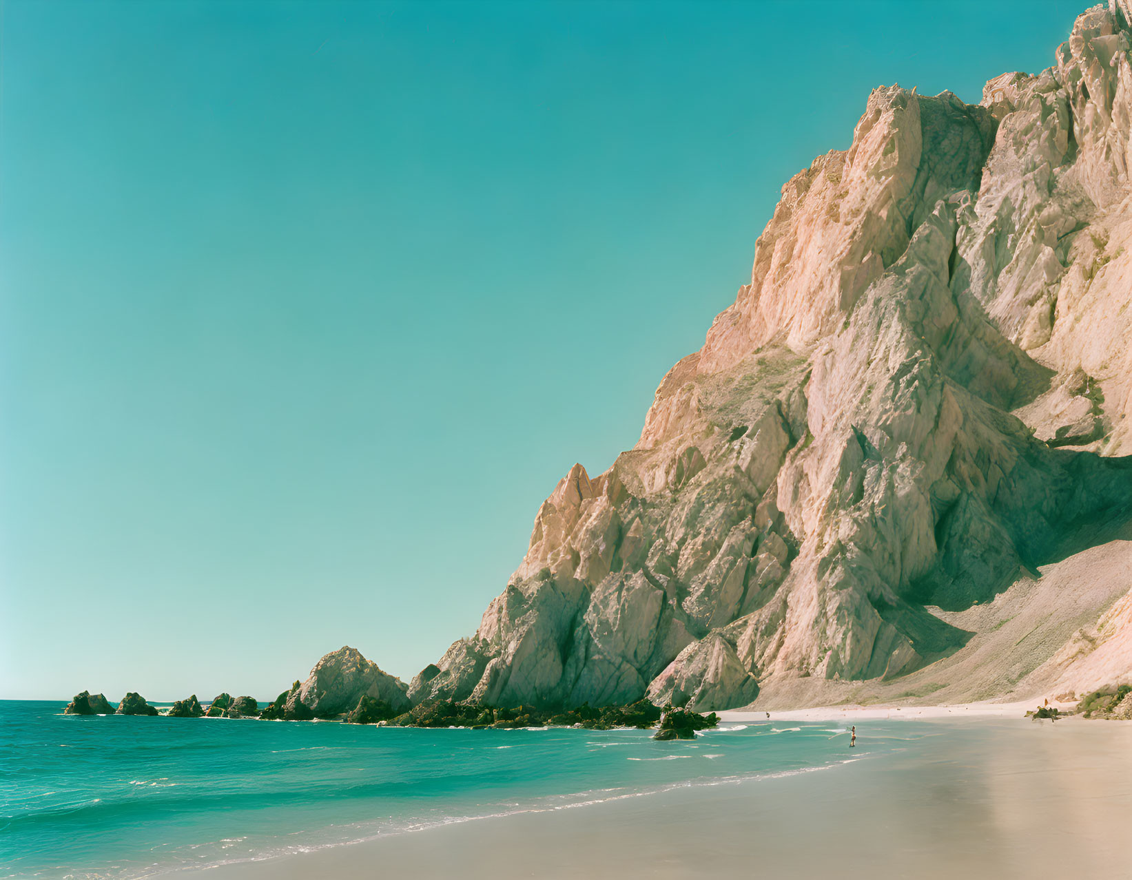 Tranquil Beach Scene with Clear Water, Sandy Shore, and Rugged Cliff