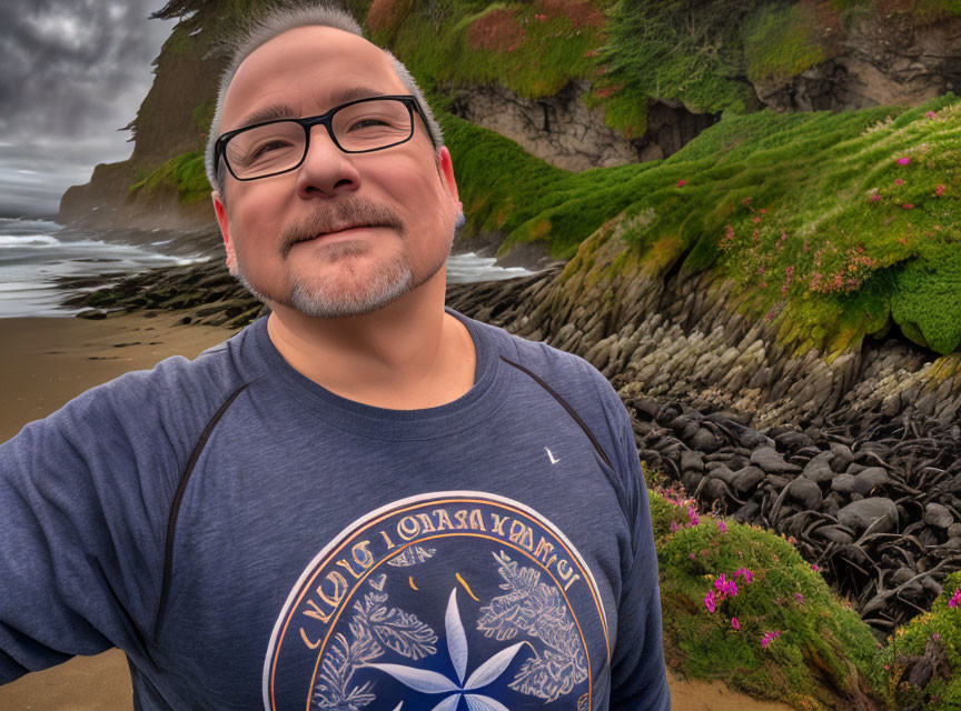 Bearded man smiling on rocky beach with greenery in background