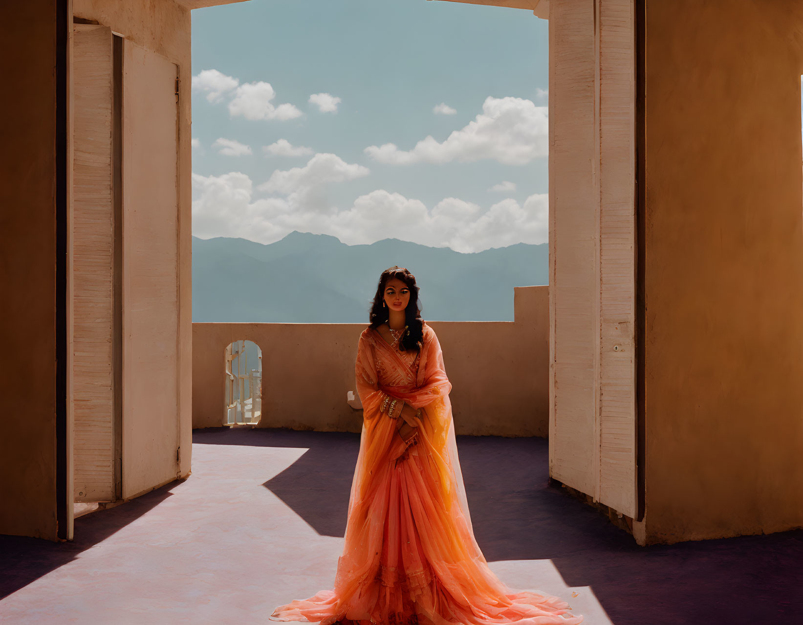 Woman in orange saree under archway with mountain backdrop