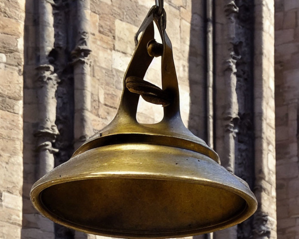 Brass bell on metal chain near stone building with sculpted details