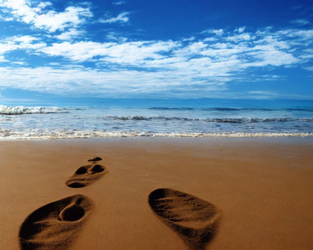 Tranquil beach scene with footprints, gentle waves, and blue sky