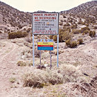 Desert landscape at dusk with blue-green vegetation and unreadable sign with red rocky outcrop