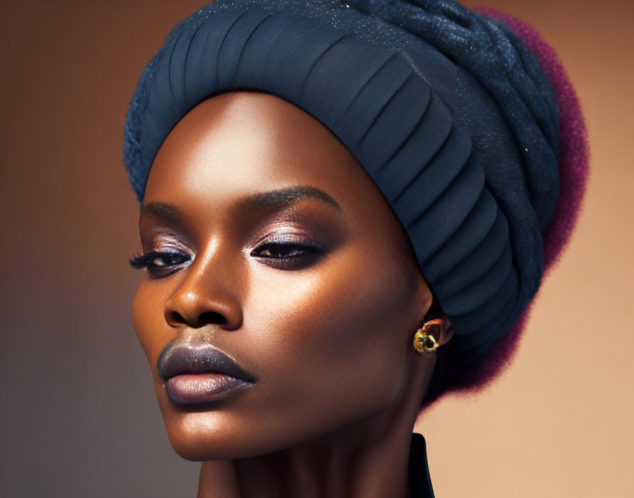 Portrait of woman with dark skin in blue headwrap, striking makeup, warm-toned background