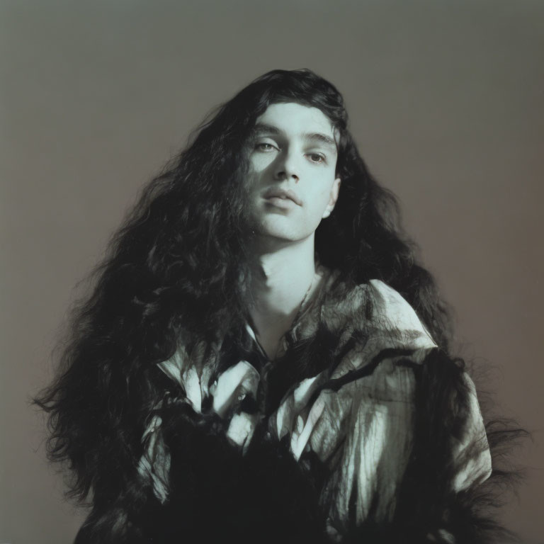 Portrait of individual with long wavy hair in striped garment against plain background