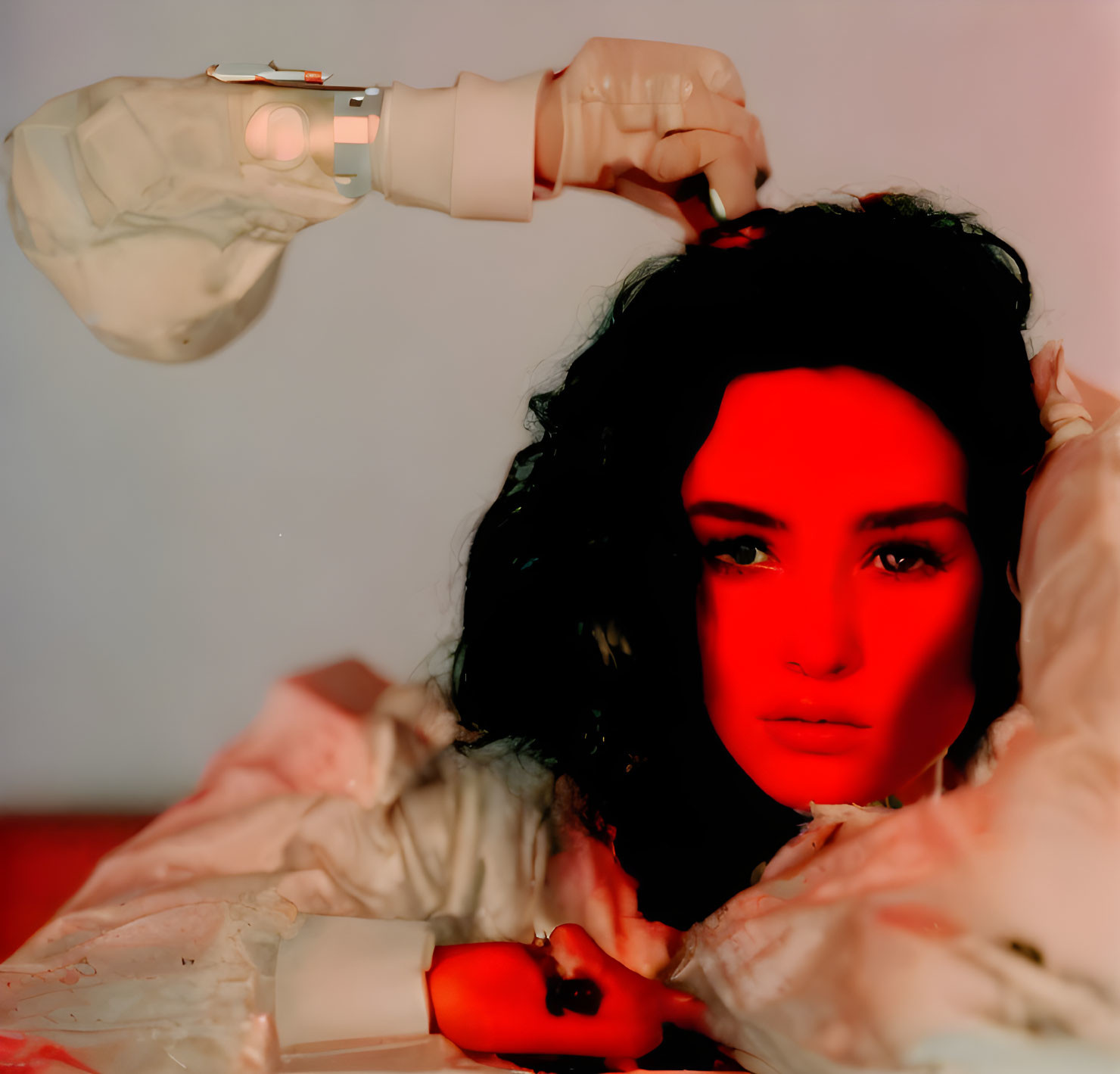 Dark-haired person with dramatic makeup lying down under red light