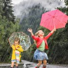 Children playing with umbrellas in rain surrounded by butterflies and cats.