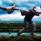 Adult swinging two children on grassy field under stormy sky