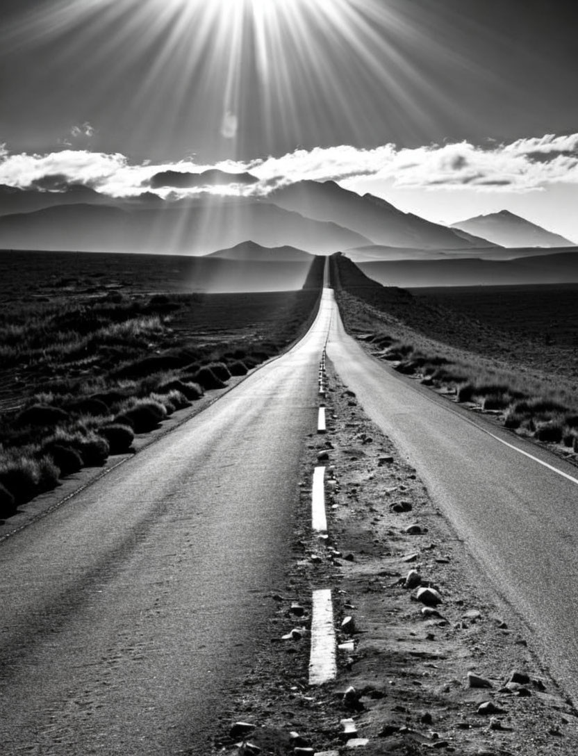 Monochrome image of straight highway to distant mountains under dramatic sky