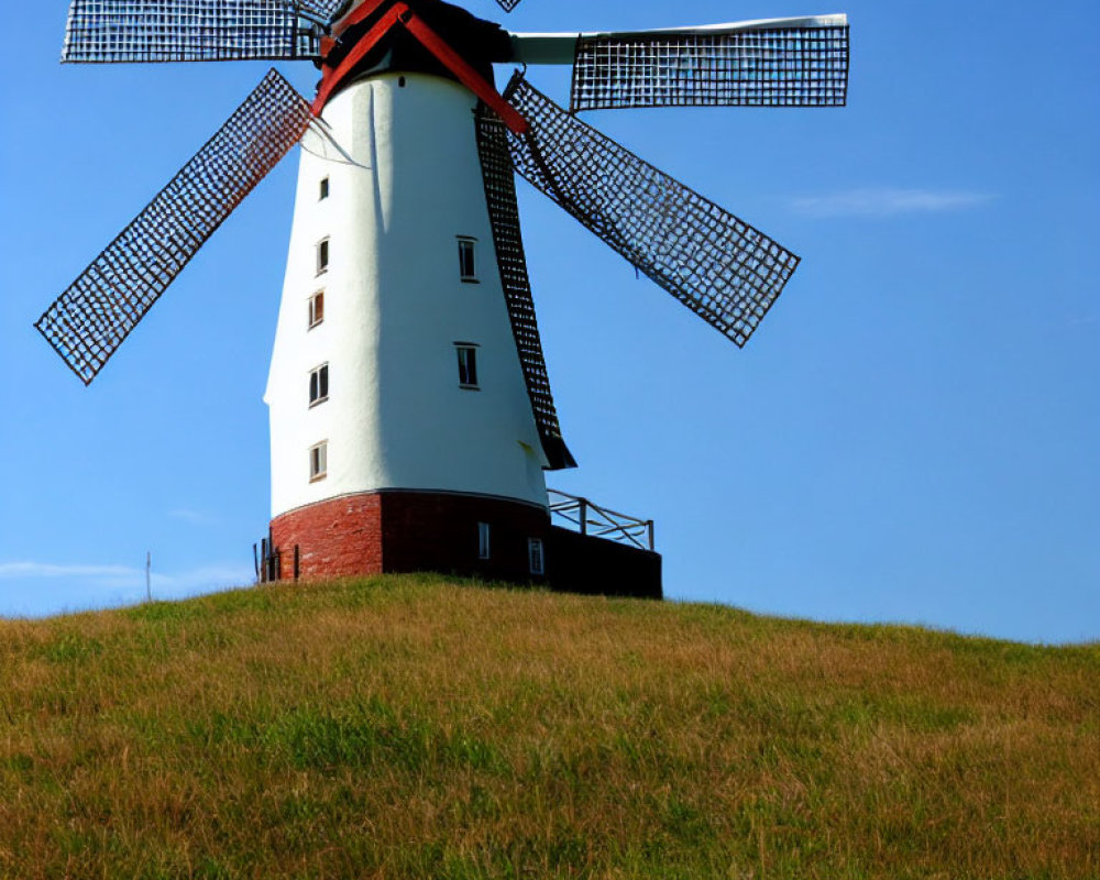 Traditional windmill with red vanes on lush green hill, clear blue sky