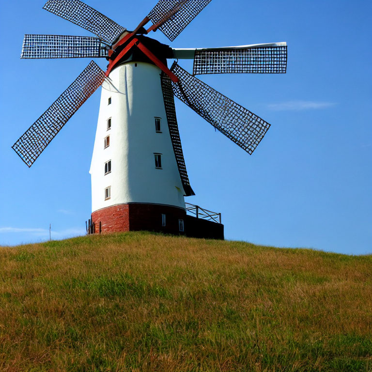 Traditional windmill with red vanes on lush green hill, clear blue sky