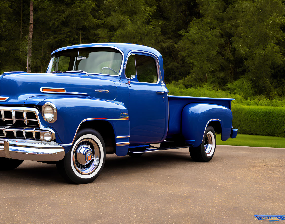 Vintage blue pickup truck with chrome details and white-wall tires on grassy road